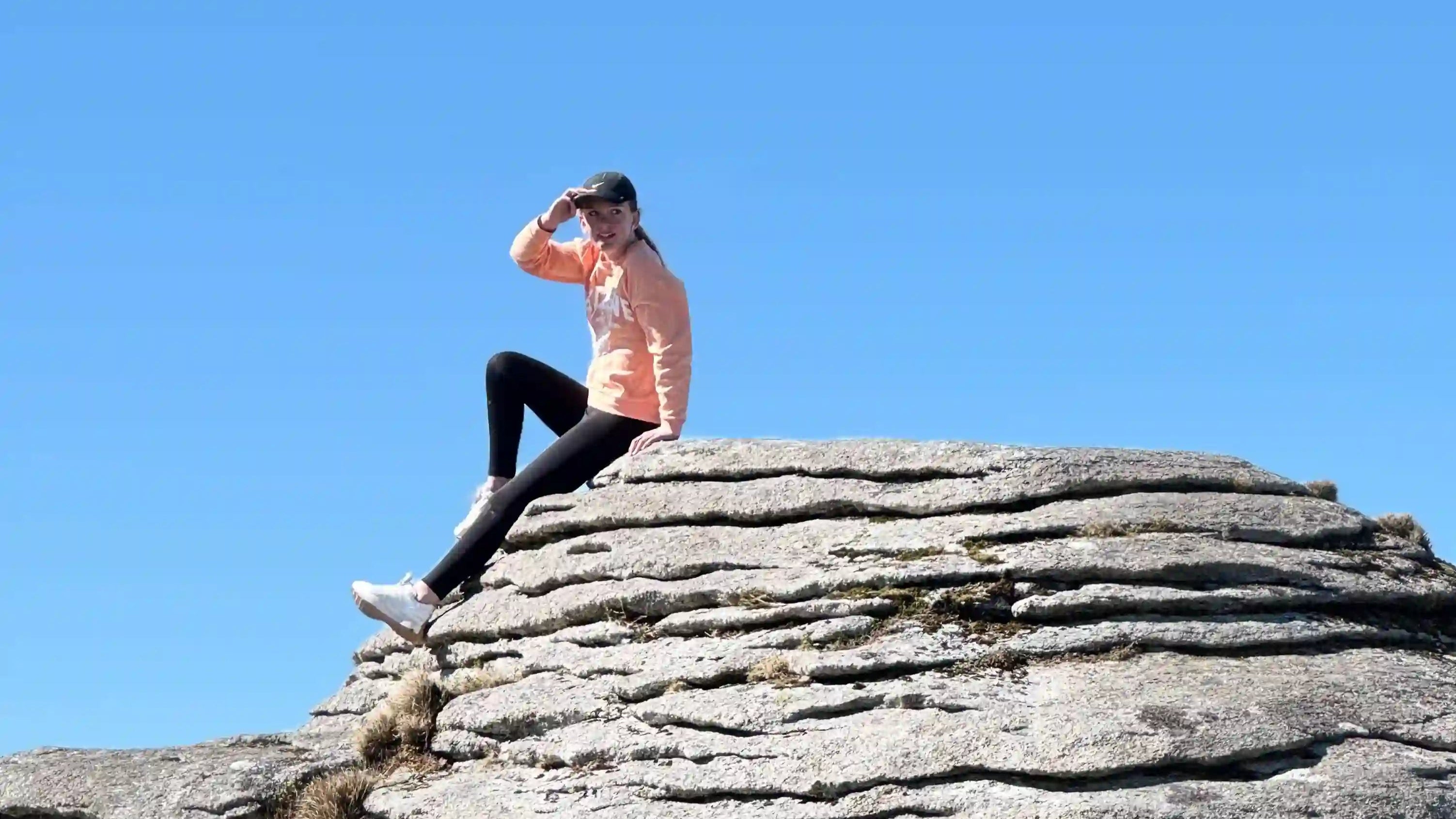 girl sat on a rock set against a blue sky