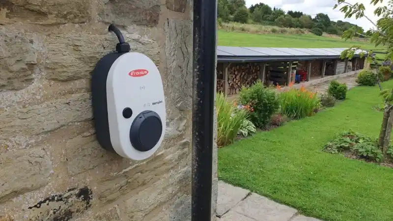 fronius car charger mounted on a stone wall near a barn with solar panels
